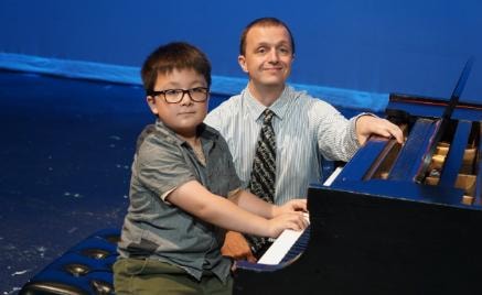 Young student and teacher at a grand piano on stage